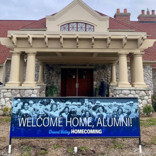 Alumni House exterior with banner, Welcome Home, Alumni, Grand Valley Homecoming on lawn in front.